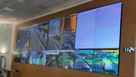 Sam Read/BBC The National Highways control room in South Mimms has a grid of cameras on the wall showing the major A roads and motorways in the East.