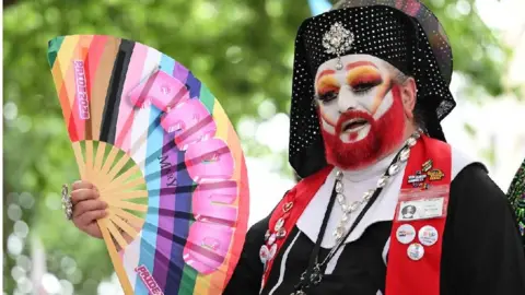 Matthew Horwood/Pride Cymru A person wearing make up, with a red beard, holding a fan with rainbow colours on it