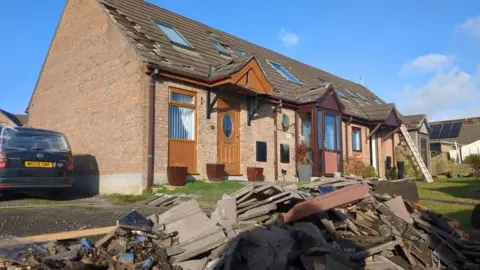 House with roof tiles missing, and tiles piled up in front