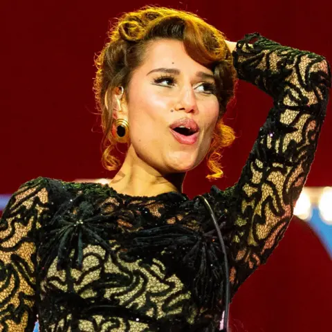 Getty Images Raye smiles as she performs on stage in a black ballgown