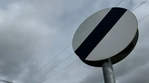 A close-up of a national speed limit sign showing a white circle with a diagonal black stripe.