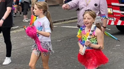 Two young girls wearing colourful clothes and carrying flags