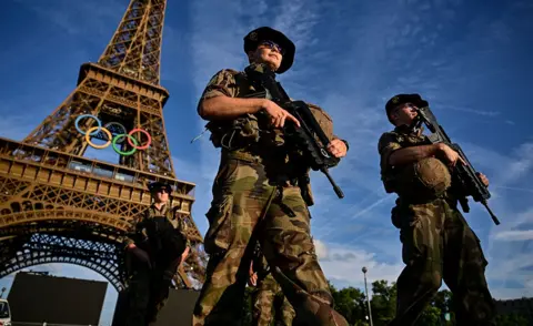 AFP French soldiers walk in Paris holding guns with the Eiffell Tower in the background displaying the Olympic games logo