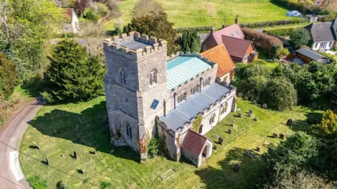 A 12th century stone church seen from above. It is sat in a churchyard surrounded by graves.