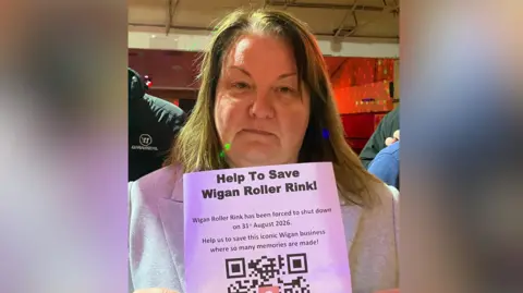 Dawn Holding holding a piece of paper reading: 'Help to save Wigan Roller Rink' with others.