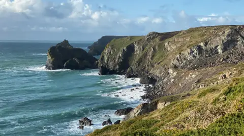 BBC A section of the Cornish coastline, with granite cliffs, gorse, grass and a blustery sea