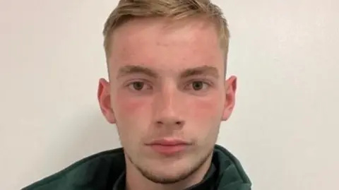 LinkedIn Headshot of Jamie Kadolski looking directly at the camera. He wears a green fleece with the collar turned up. She has short blonde hair. 