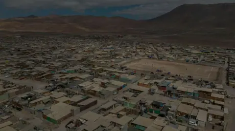 Getty images a airline showing a dense collection of houses and a playground of the ground on the side of the hilllifting paws, cylum. The plan seems dry and powder and there are stimane mountains in the background  