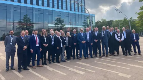Laura Coffey/BBC Group of Reform UK councillors for North Northamptonshire Council wearing suits standing outside the council offices at the Corby Cube.