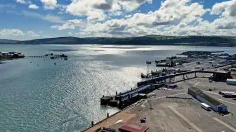 The port of Larne on a bright day. There are hills in the distance and white clouds in the sky.