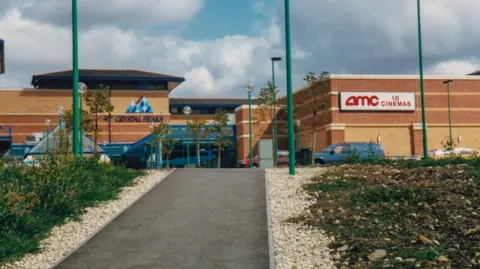 supplied A brown brick shopping centre and car park. A sign reads 'AMC 10 cinema'