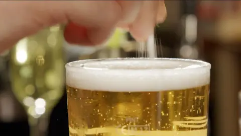 White powder being sprinkled from someone's hand into a pint of beer