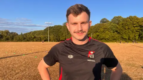 Dominic Mickleburgh is on a rugby field wearing a black and red Vigo RFC shirt
