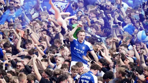 PA Media Ipswich's George Edmundson his held aloft above a crowd on the Portman Road pitch