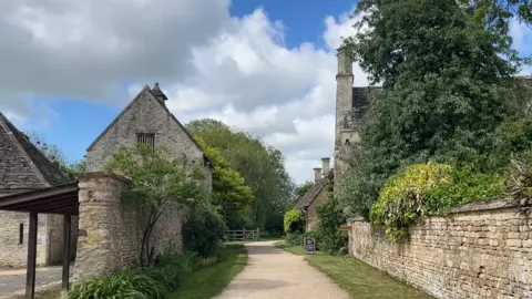 A view of the grounds of Kelmscott Manor and its buildings. It is cloudy.