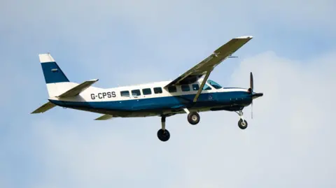 Alamy A blue and white Cessna plane with the serial number G-CPSS on the site. Its wheels are down and there is a propeller at the front.