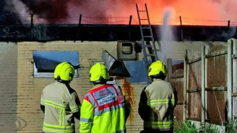 Three firefighters watch the blaze at the derelict social club