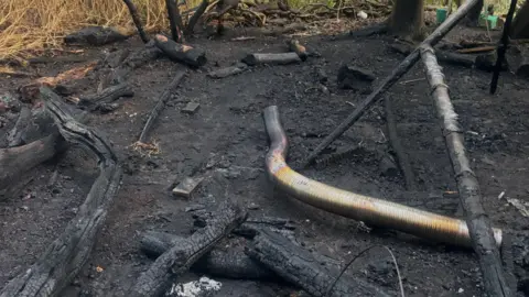 Little Wild Tribe A large metal pole and burned branches lying on a charred floor.