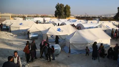 EPA People standing around tents at a shelter, north of Idlib city (28/11/24)