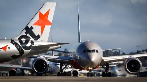 The tail and nose of two Jetstar planes on the runway at Sydney International Airport