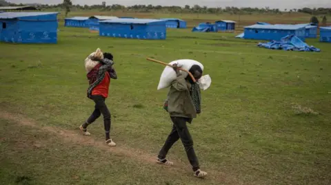 AFP Two internally displaced persons (IDPs) carry supplies back to their tents after a food distribution at the Mai-Dimu IDPs camp outside Shire, Tigray region, on July 15, 2024. 