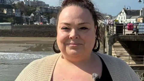 Charmain Lovett in a black top and a beige cardigan with Ilfracombe harbour in the background