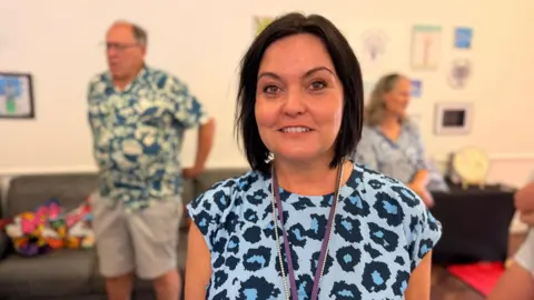 A women with short black hair cut into a bob style. she is wearing a blue leopard print top and looking at the camera smiling.