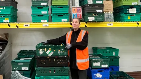 Julia Gregory/BBC A woman is surrounded by shelves of donated food in a warehouse