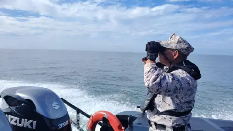 Malaysia Coast Guard A Malaysian Coast Guard official on  a boat uses binoculars to search the water 