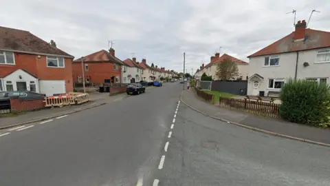 A generic photo showing Regent Street going from the bottom left to the centre of the photo. It is pictured at the junction with Pine Tree Road, which is on the right. Houses and cars are on both sides of Regent Street.  