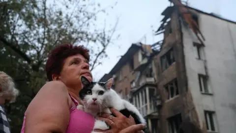 A woman holds a cat in front of a building in Kyiv hit by a Russian shell on 10 July