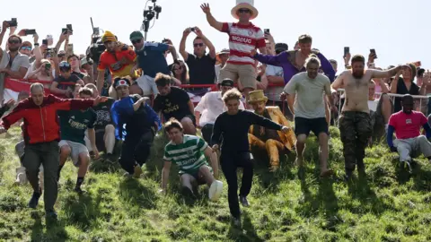 PA Media Dozens of men begin a downhill race at the Gloucestershire cheese rolling event. The picture is taken from below looking up the slope