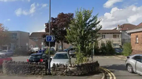 Image of an urban car park in the Staple Hill area of Bristol showing several parked cars, surrounded by residential housing.