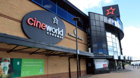 The outside of a Cineworld Cinema complex. A logo of the company is on the outside of the building which is a black oval with a white star and red and white writing which says cineworld CINEMAS.