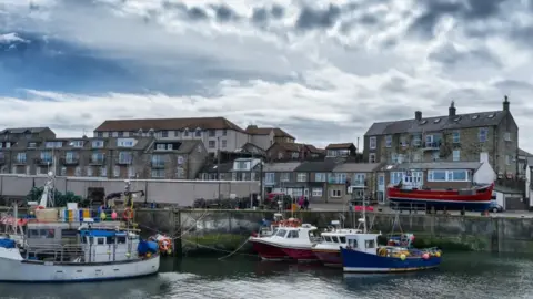 Gordon Bell/Getty Images A picture of the harbour at Seahouses with boats moored up and rows of houses behind 