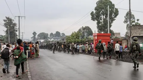 AFP Armed men in military uniform, from the M23 rebel group walk through a street of the Keshero neighbourhood in Goma, as crowds look on