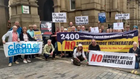A group of around 20 protesters standing outside a Town Hall. They are holding up banners and placards indicating their opposition to an incinerator.