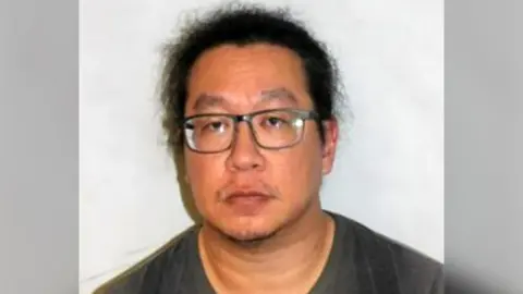 Photo of Chan wearing glasses against a plain background, in a passport-style photograph.