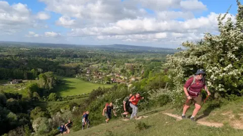 A group of men climb up a very steep hill that overlooks a small village. 
