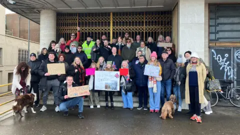 Cash Murphy/BBC Protesters stood at the entrance to Dreamland, Margate. Around 40 people can be seen in the image with a number of signs and two dogs.