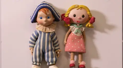 Jason Lock Props of Andy Pandy in a blue and white striped hat and onesie-type suit. Next to him is female character Looby Loo, who has blonde plaits and a pink spotted dress.