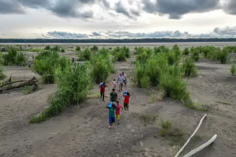 Luis Acosta/AFP An aerial view of Yagua indigenous people carrying water and other goods due to the falling level of the Amazon River on Isla de los Micos, Amazonas Department, Colombia, on October 4, 2024. 