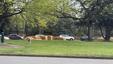 Rachael McMenemy/BBC A number of hay bales on the other side of a roundabout. Cars pass alongside the bales. 