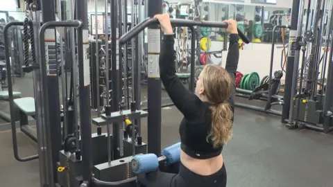 Issy Hart pulling down a bar on an exercise machine in the gym at the University of Plymouth