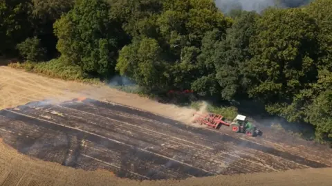 Josh Corrie A tractor ploughing an area next to to a fire in woodland and burnt crops