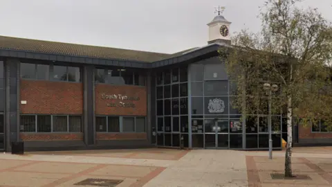 The red brick and glass court building of South Tyneside Magistrates' Court. There is a square in front of the site, with a small willow tree growing at its centre.
