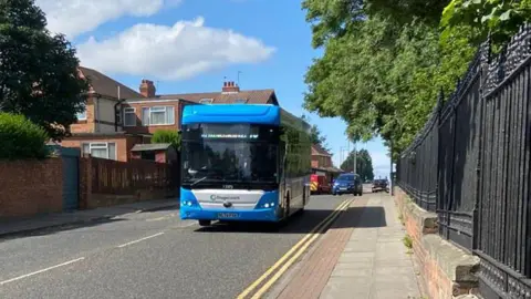 BBC Blue Stagecoach bus driving along road on sunny day with trees on both sides. 