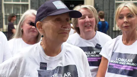 A woman wearing a navy blue cap with a logo on it reading "Lobular Moon Shot Project". The woman was a breathing tube attached to her nose.