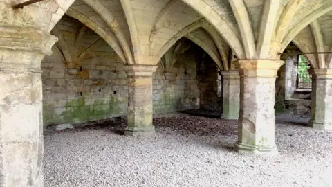 Kit Taylor/BBC Large medieval stone pillars with gravel floor.