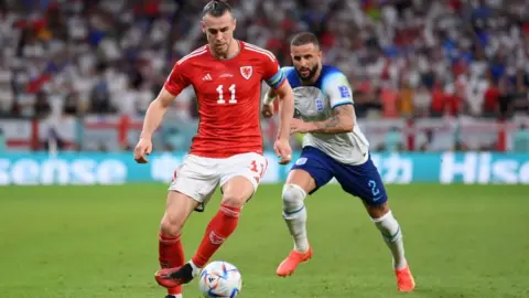 Getty Images Gareth Bale, wearing the red 11 shirt, white shorts and red socks of Wales, controls the ball, pursued by Kyle Walker, wearing the white and blue shirt, blue shorts and white socks of England.